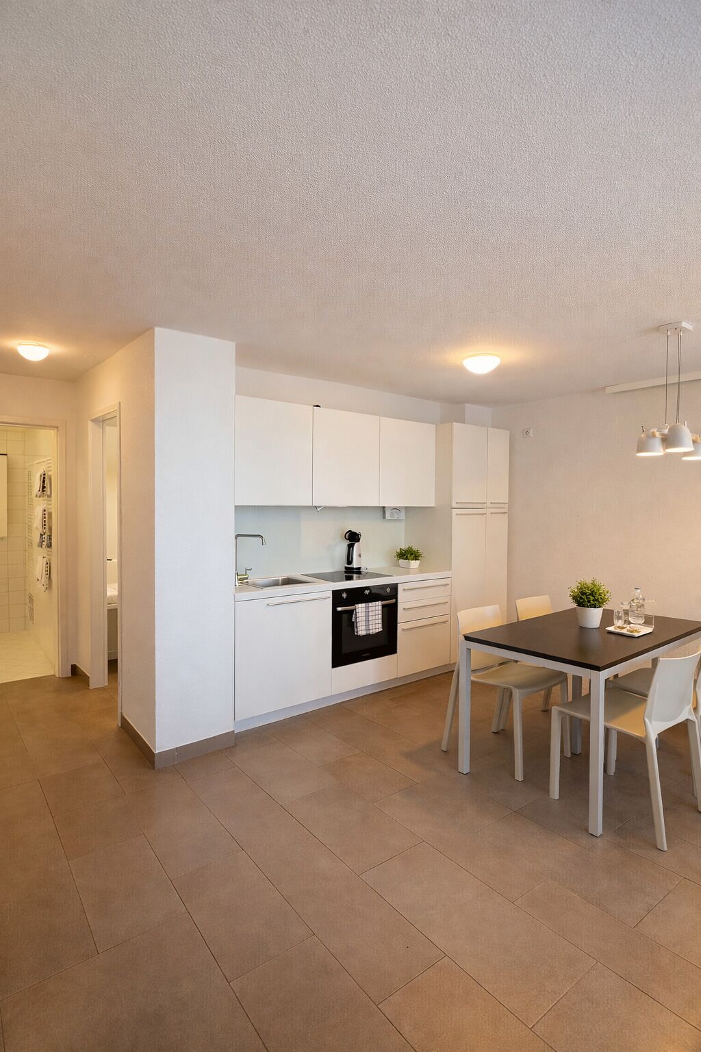 A modern kitchen with white cabinetry, a built-in oven, and a dining area with a table and chairs.