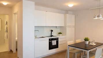 A modern kitchen with white cabinetry, a built-in oven, and a dining area with a table and chairs.