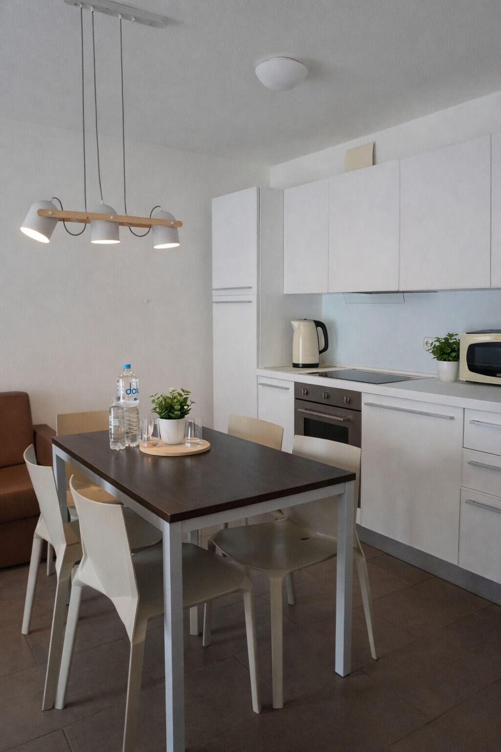 Une cuisine moderne avec des armoires blanches, un four en acier inoxydable et un four à micro-ondes. On y trouve une table à manger avec des chaises et une plante en pot posée sur la table.