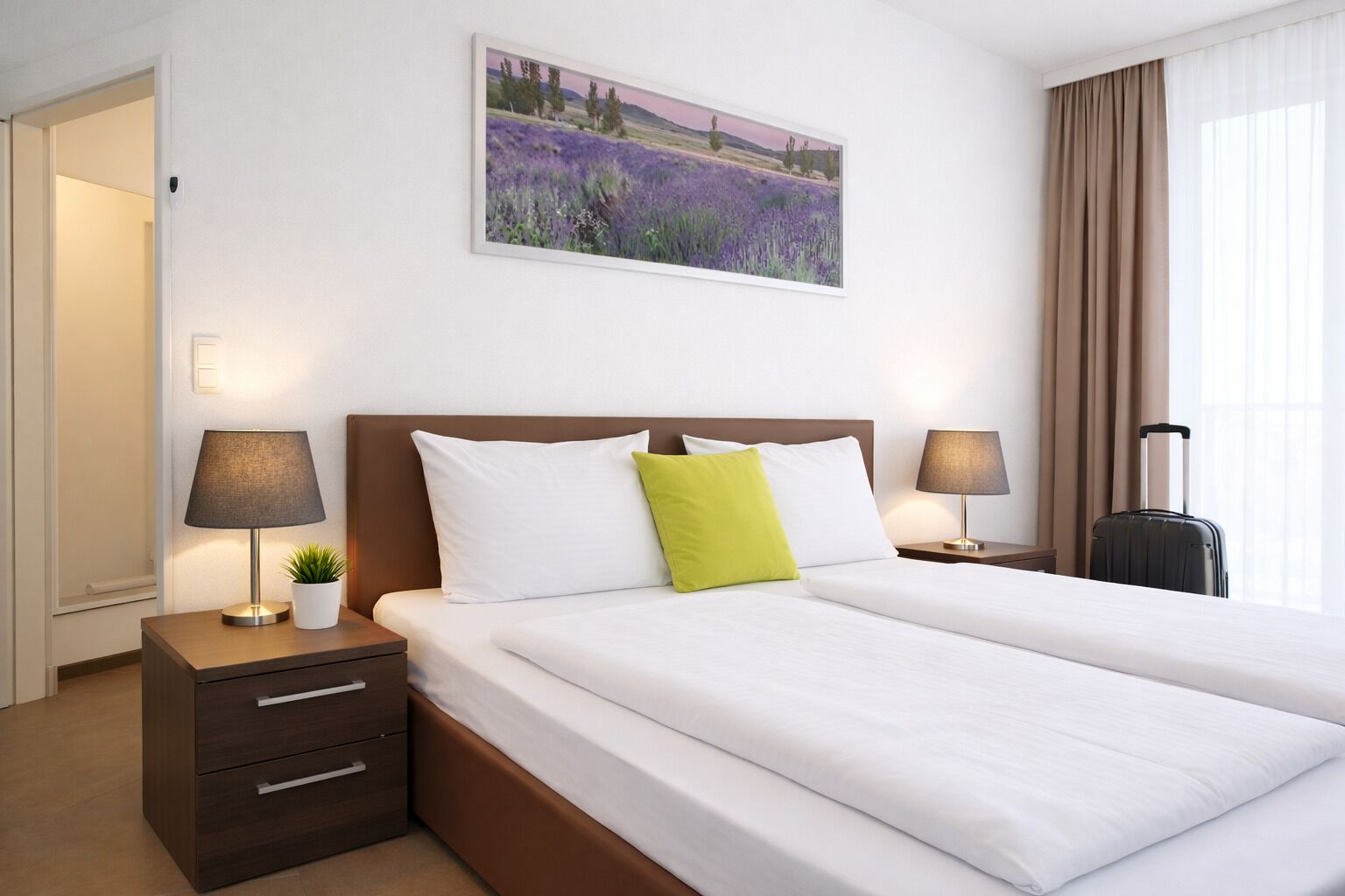 A hotel room with a large bed, two bedside tables with lamps, a small potted plant, and a painting of a field on the wall.