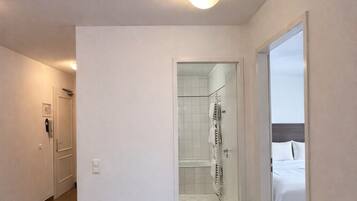 Una habitación de hotel con cama, una planta en maceta y un baño con ducha y toallero.