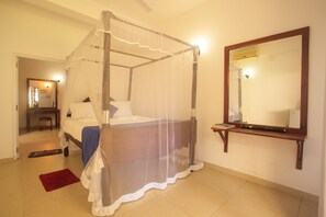 A bedroom with a four-poster bed, a bedside table, a mirror, and a red rug.