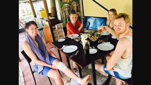 Un grupo de personas sentadas en una mesa con platos, vasos y una botella.