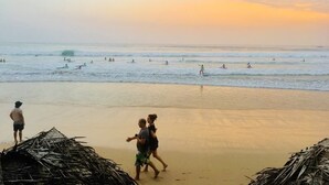 Una playa con gente nadando y caminando, y cabañas de techo de paja al frente.