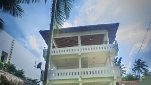 Un edificio de dos pisos con un balcón, rodeado de césped y palmeras.