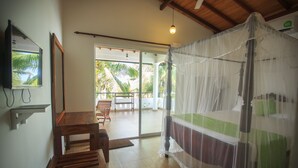 Una habitación con una cama cubierta por una mosquitera, un banco de madera, una mesa y vistas a palmeras a través de una puerta de cristal.