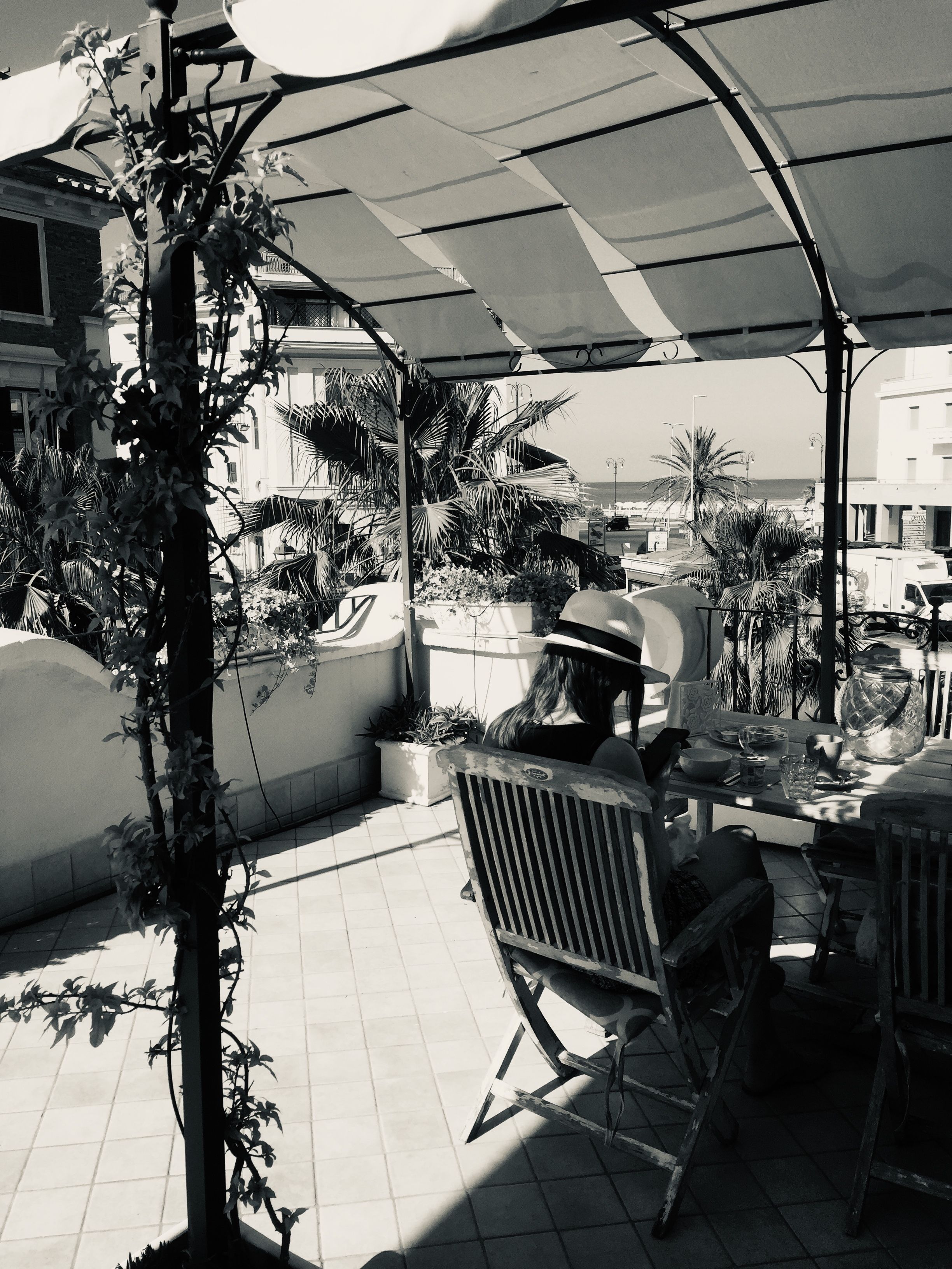 An outdoor patio area with a table and chairs, surrounded by potted plants and a large umbrella providing shade.
