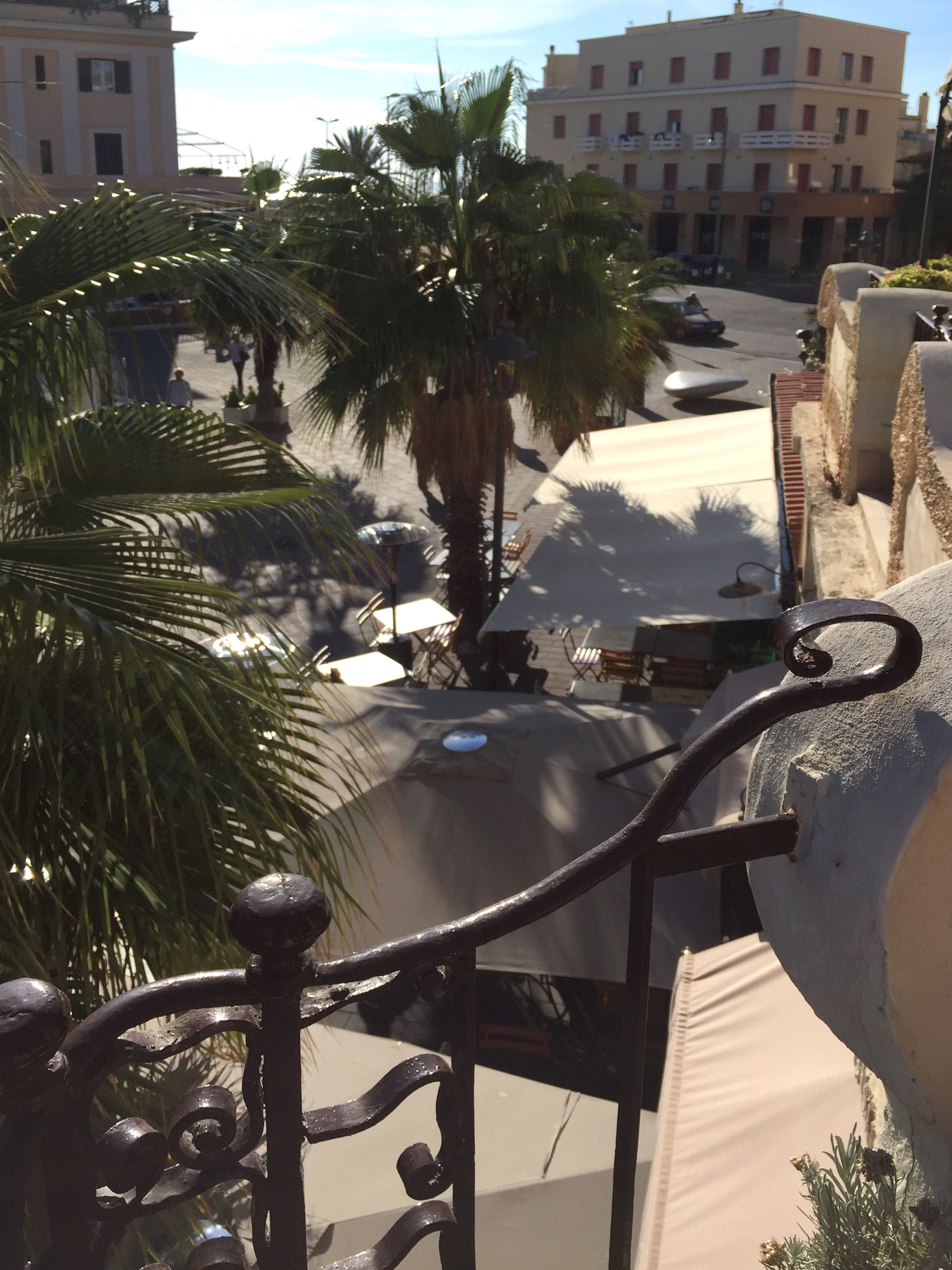 Vista de la calle con palmeras, un café y edificios al fondo.
