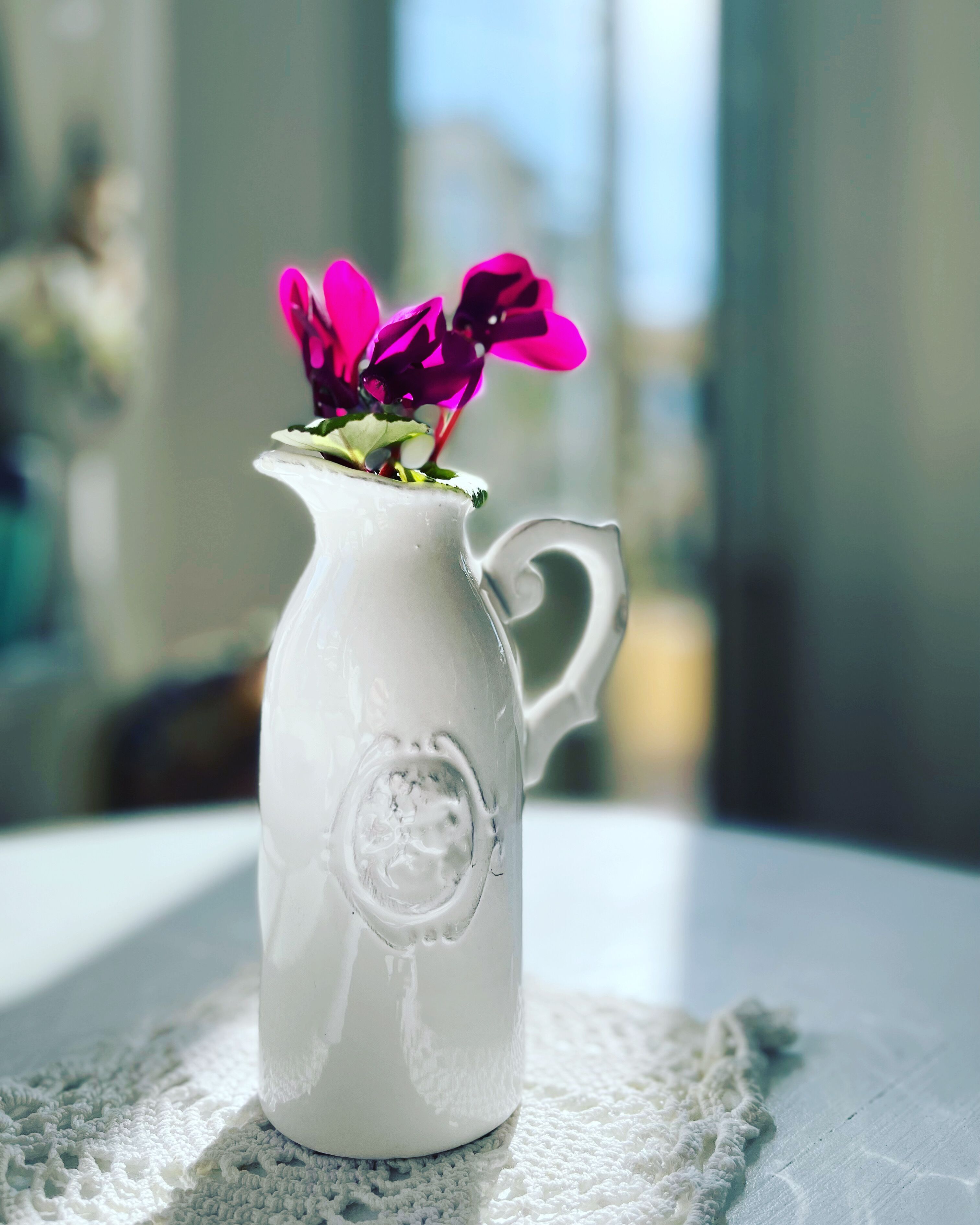 A white ceramic pitcher with a handle, placed on a lace doily.