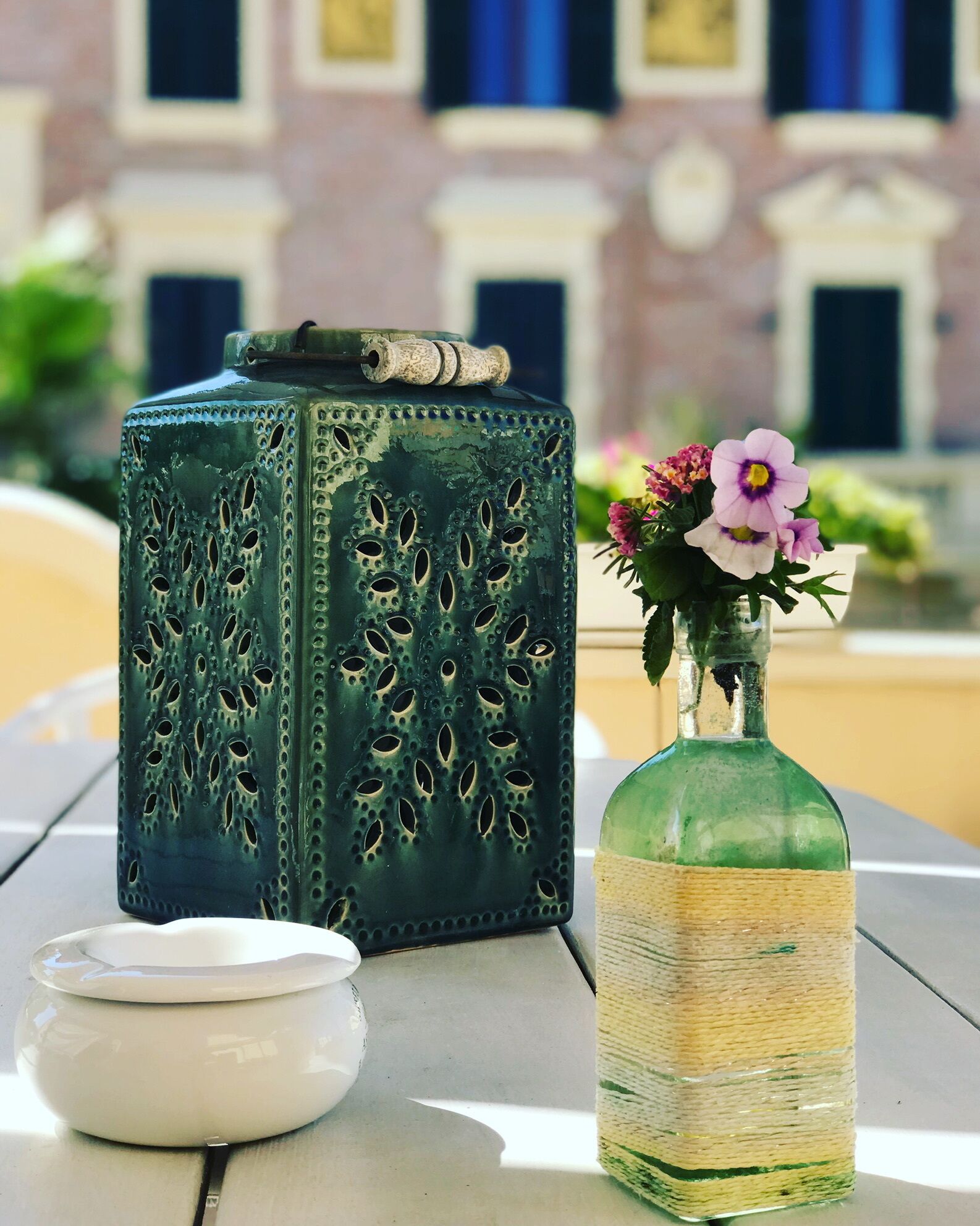 A green decorative box with a handle, a clear glass bottle with a woven band, and a white ceramic container on a table.