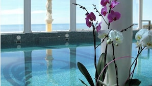 Een binnenzwembad met helder water, een witte sculptuur en orchideeën.