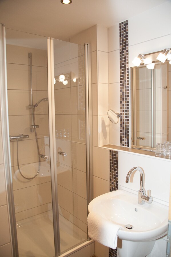 A modern bathroom with a glass-enclosed shower, a white sink, and a mirror with lights above it. - Ferienhof Bettmann (Ennigerloh)