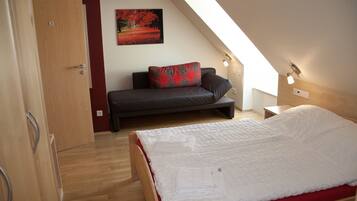 A bedroom with a bed, a sofa, a painting, and a skylight.