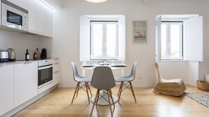 Een moderne keuken met witte kasten, een inbouwoven en een eethoek met een ronde tafel en twee stoelen.