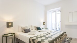 Een slaapkamer met een bed, twee nachtkastjes, een lamp, een deken en uitzicht op buiten.