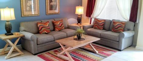 A living room with a grey sofa, colorful cushions, a wooden coffee table, and a striped rug.