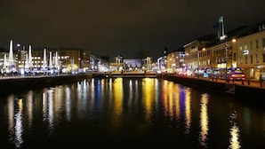 A nighttime view of a city waterfront with illuminated buildings and a bridge.