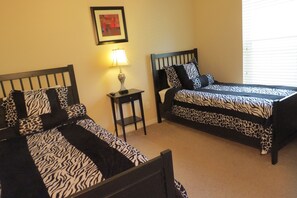 A bedroom with two beds, each with zebra-patterned bedding, a nightstand with a lamp, and a framed picture on the wall. - Westridge Area Pool Home (Davenport)