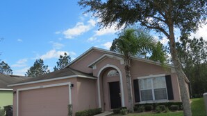 A single-story house with a garage, a front door, and a small front yard with a palm tree and shrubs. - Westridge Area Pool Home (Davenport)