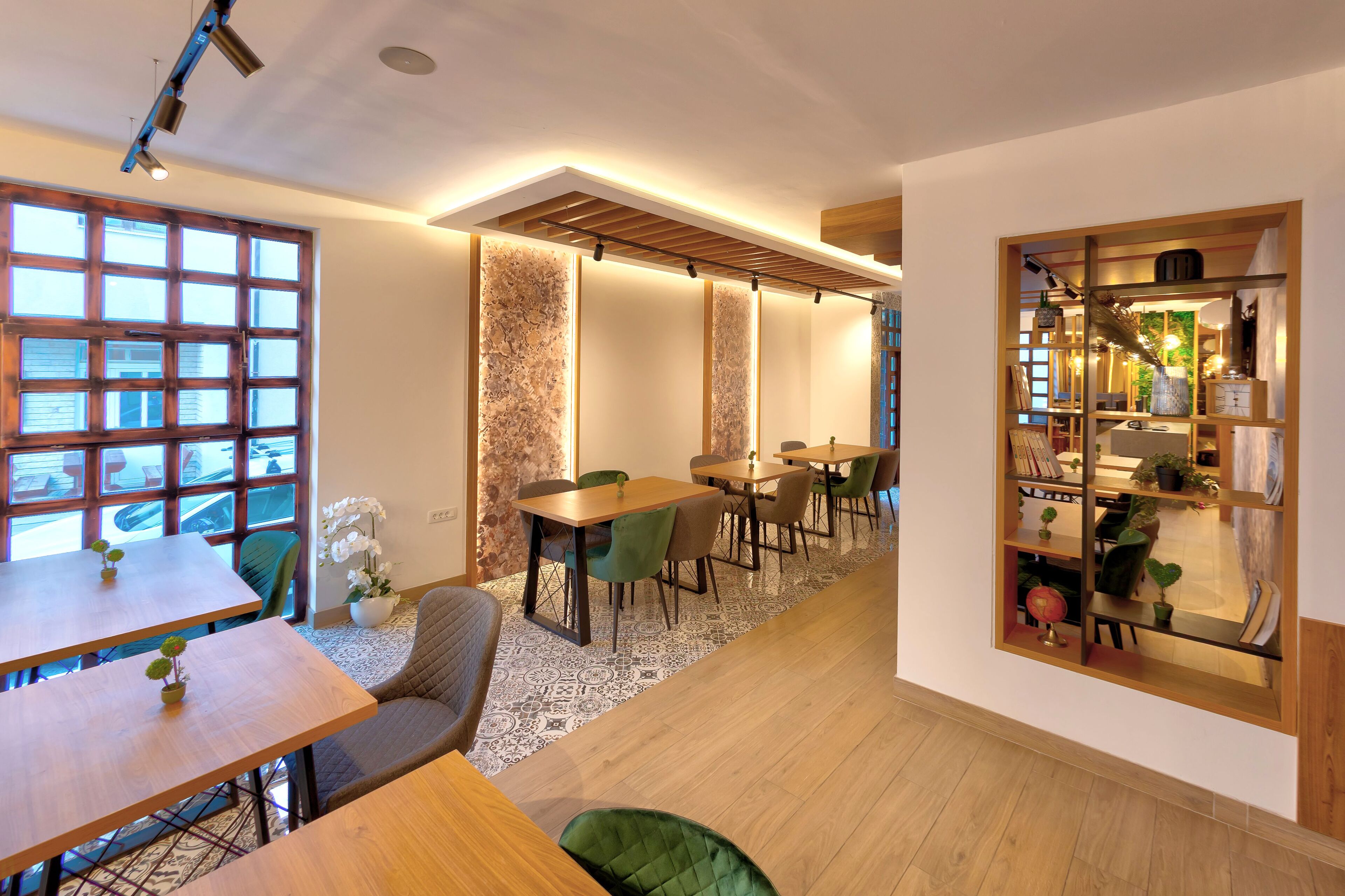 Un espace de restauration moderne avec des tables et des chaises en bois, un tapis à motifs et une vue dégagée sur l’extérieur grâce à une grande fenêtre.