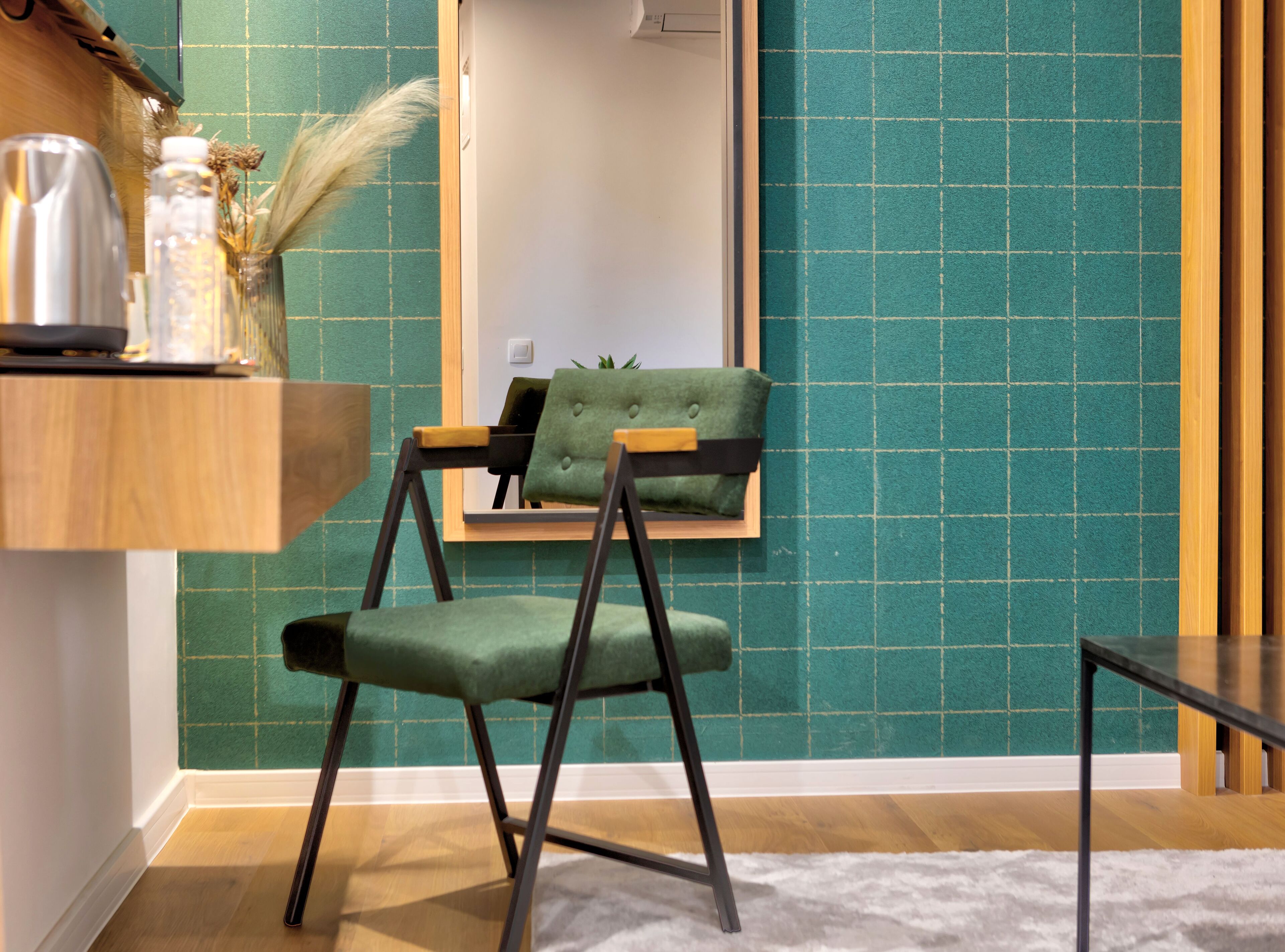 A modern room with teal walls, a wooden floor, a green upholstered chair, a small table, and a mirror.