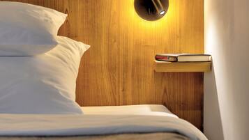 Cama bem arrumada com lençóis brancos, cabeceira de madeira e mesa de cabeceira com um livro e uma luminária.
