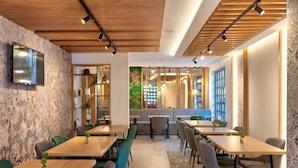 A modern dining area with wooden tables and chairs, a television mounted on the wall, and a decorative plant.