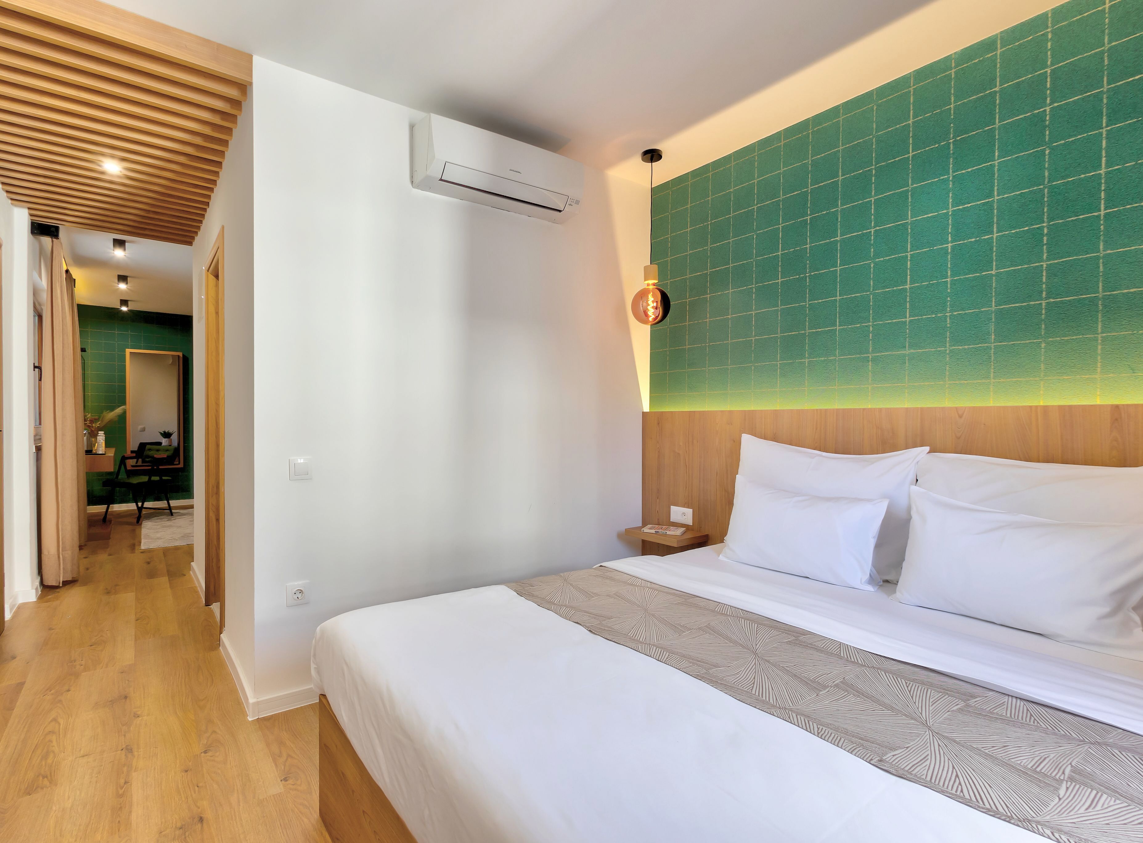 A hotel room with a bed, a nightstand, a green-tiled wall, and a wooden ceiling.