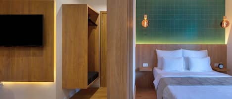 A modern hotel room with a large bed, a TV mounted on the wall, wooden furniture, and a green-tiled accent wall.
