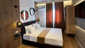 A modern bedroom with a wooden slat wall, a large bed with a brown accent, a wardrobe, and a ceiling light fixture.