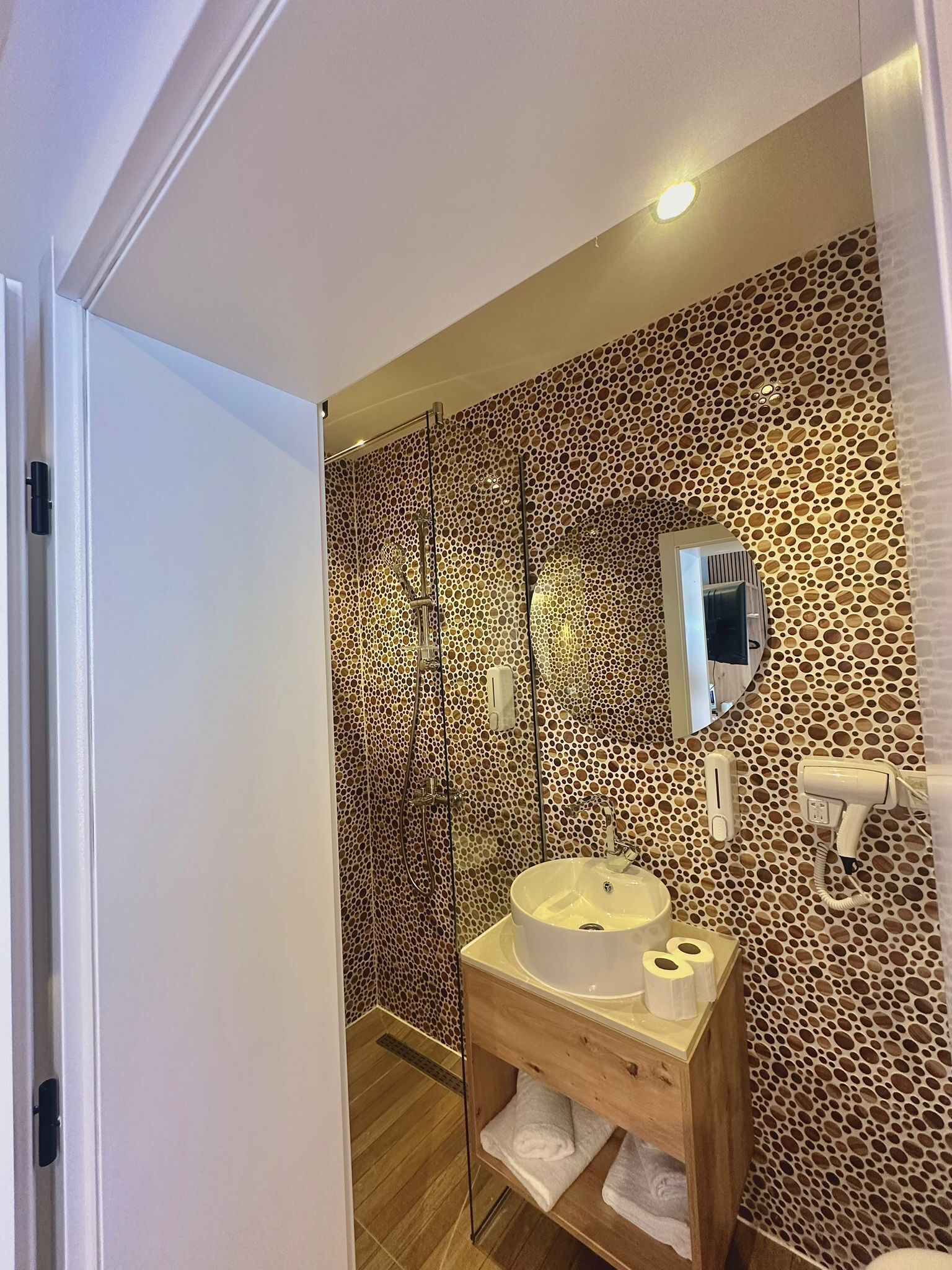 Une salle de bain avec un mur à motifs, un meuble-lavabo en bois, un évier, un miroir et un espace douche.