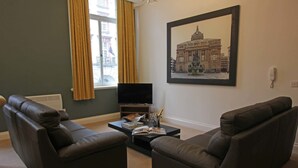 Een woonkamer met twee donkere leren banken, een salontafel met tijdschriften, een televisie en een lijst met een afbeelding van een gebouw aan de muur.