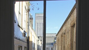 Uitzicht vanuit een raam op een smalle straat met gebouwen, een zichtbare straatlantaarn en een heldere lucht.