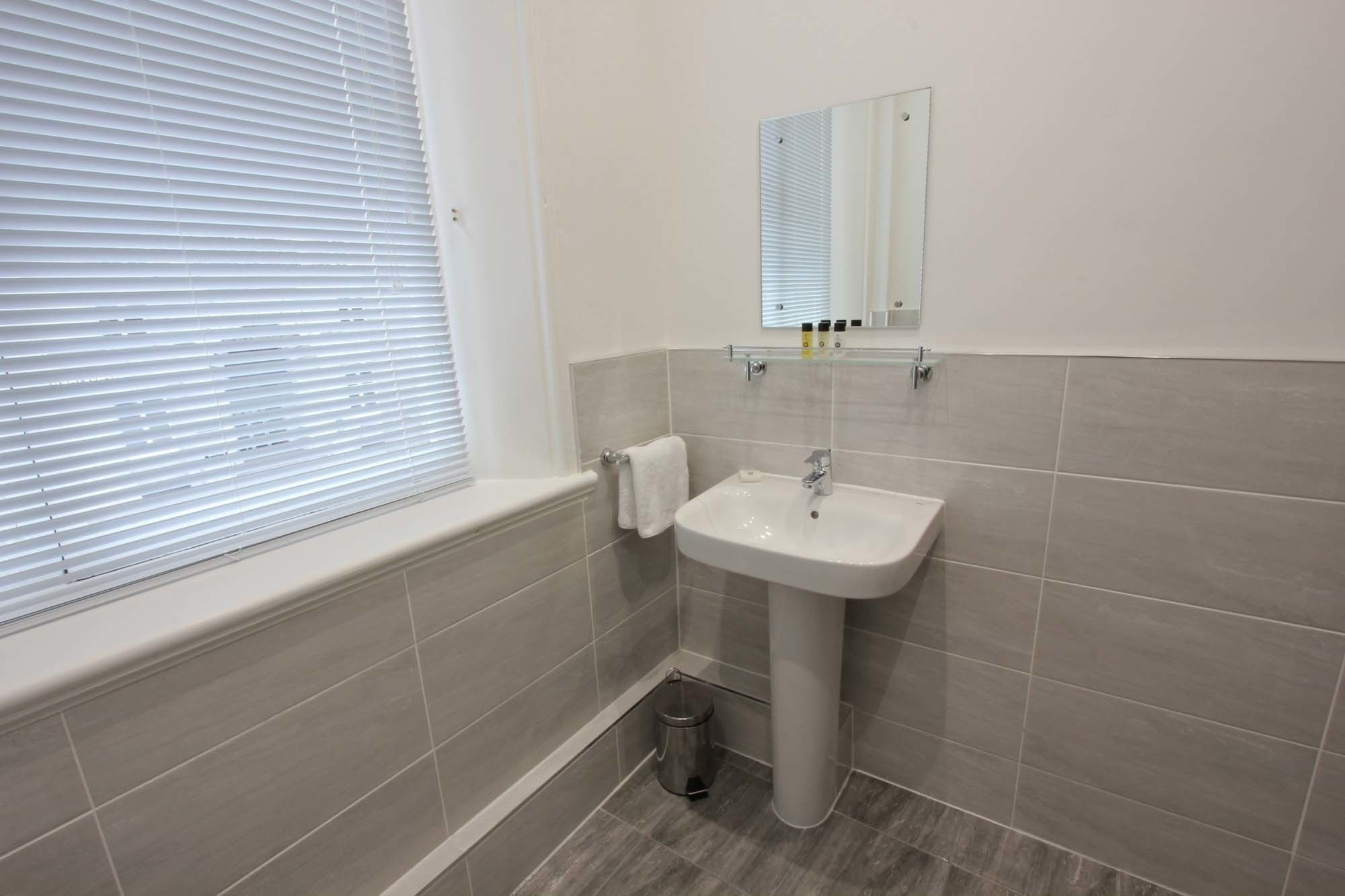 A bathroom with a white sink, a mirror, and a window with blinds.