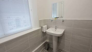 A bathroom with a white sink, a mirror, and a window with blinds.