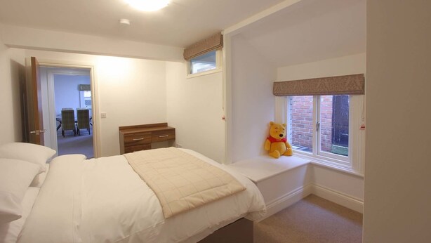 Een slaapkamer met een bed, een kaptafel, een raam met uitzicht en een knuffel op het raamkozijn.