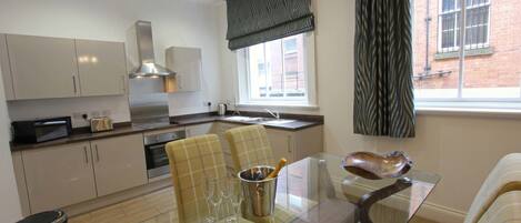 A modern kitchen with white cabinets, stainless steel appliances, and a dining area with a glass table and plaid chairs.