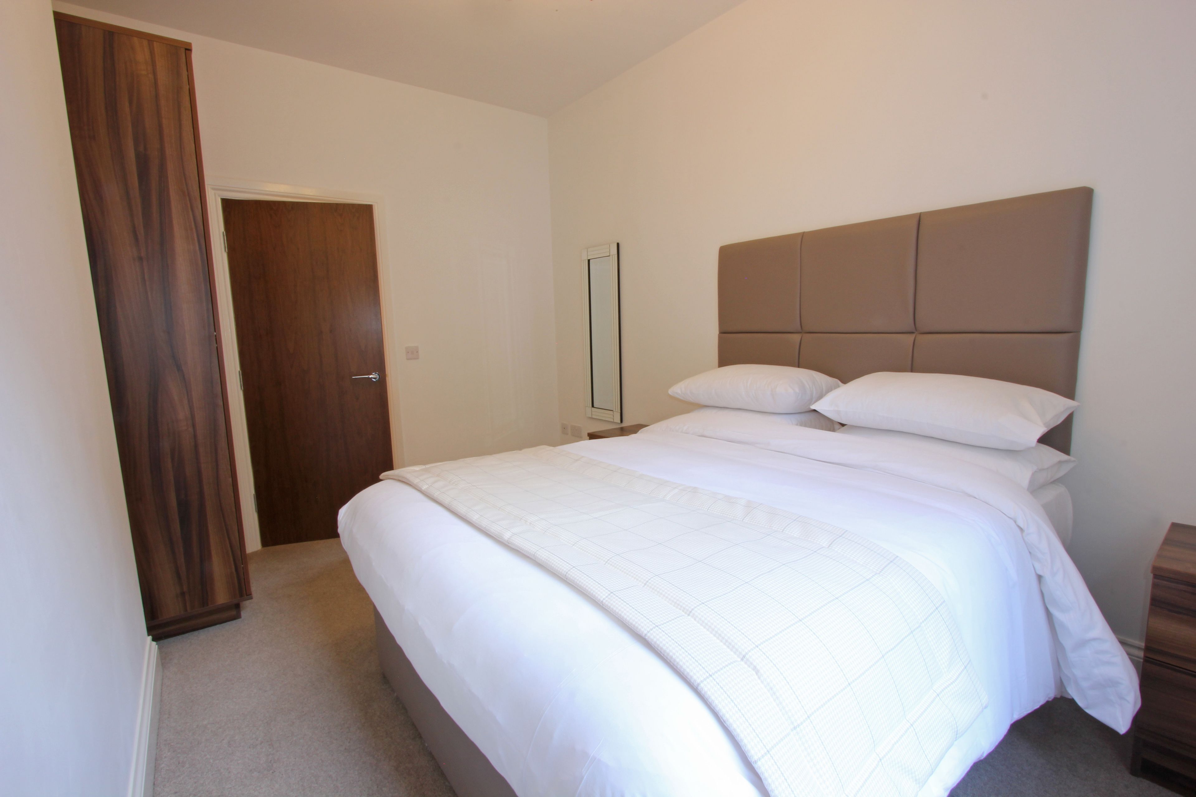 A bedroom with a large bed, a wooden wardrobe, and a mirror on the wall.