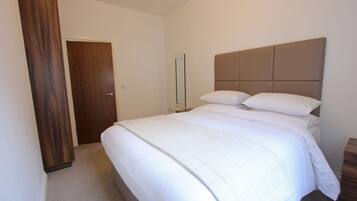 A bedroom with a large bed, a wooden wardrobe, and a mirror on the wall.