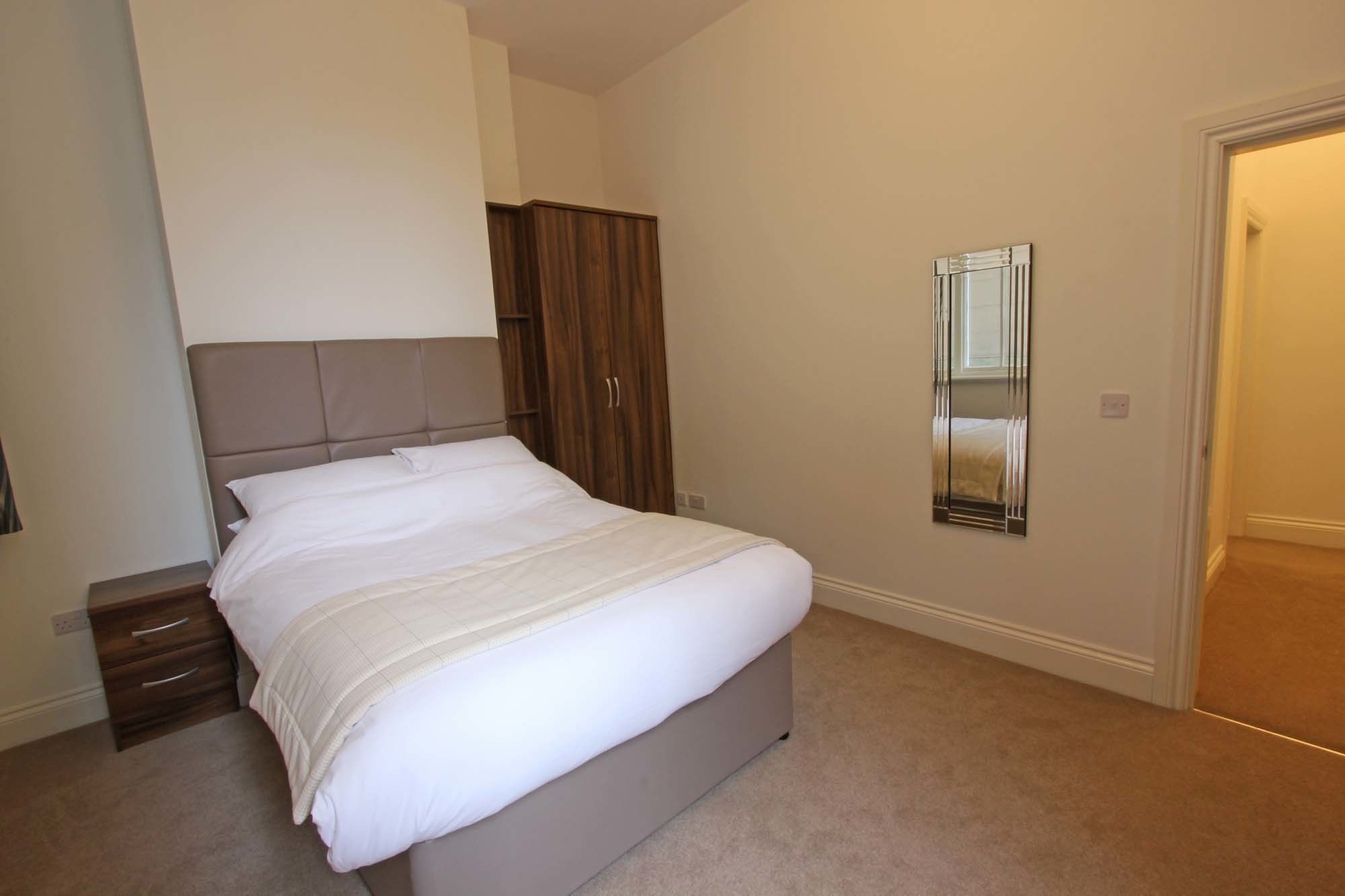 A neatly made bed in a bedroom with a wooden wardrobe and a mirror on the wall.