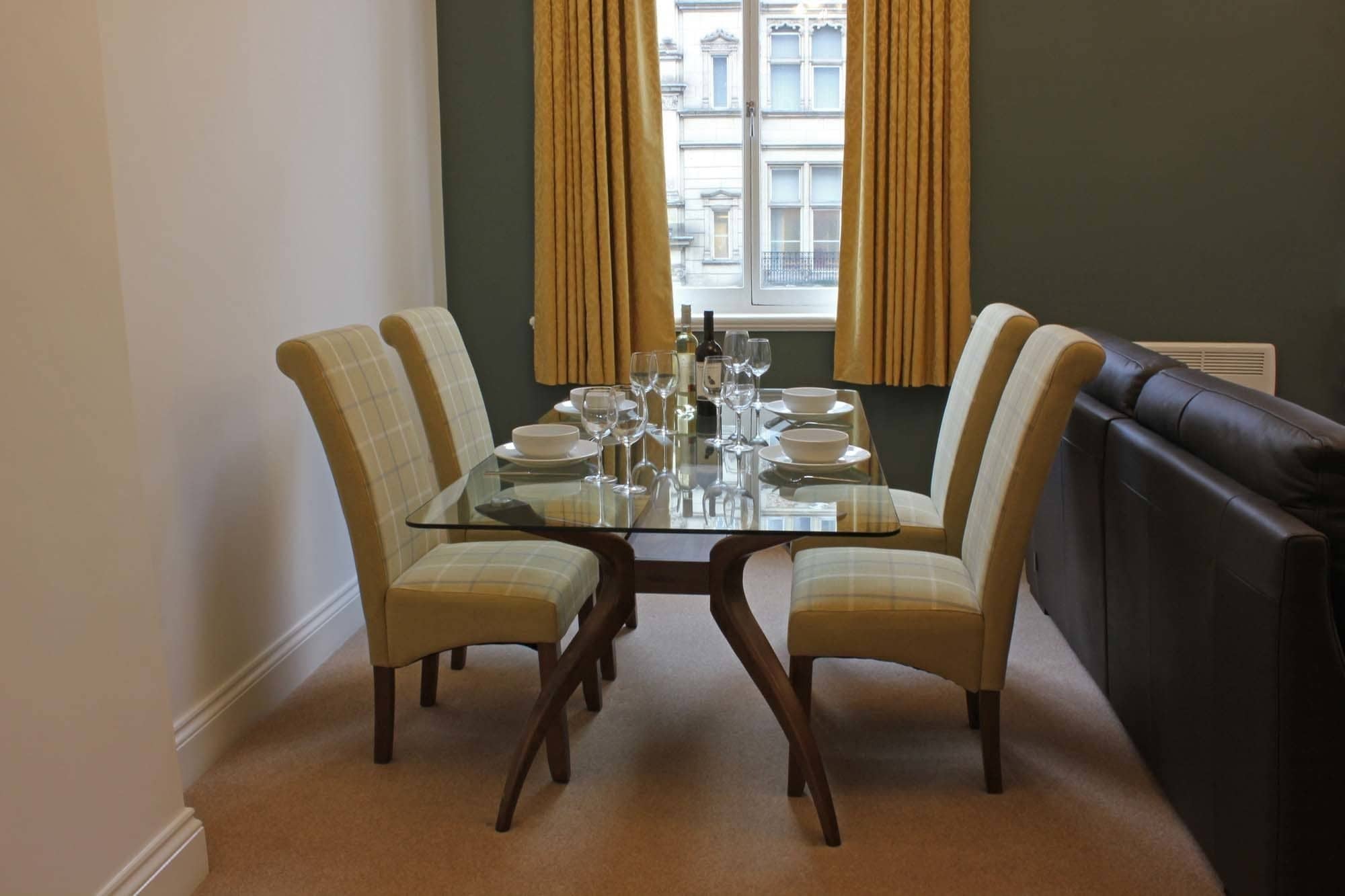 Un comedor con mesa de vidrio, cuatro sillas y un sofá negro.