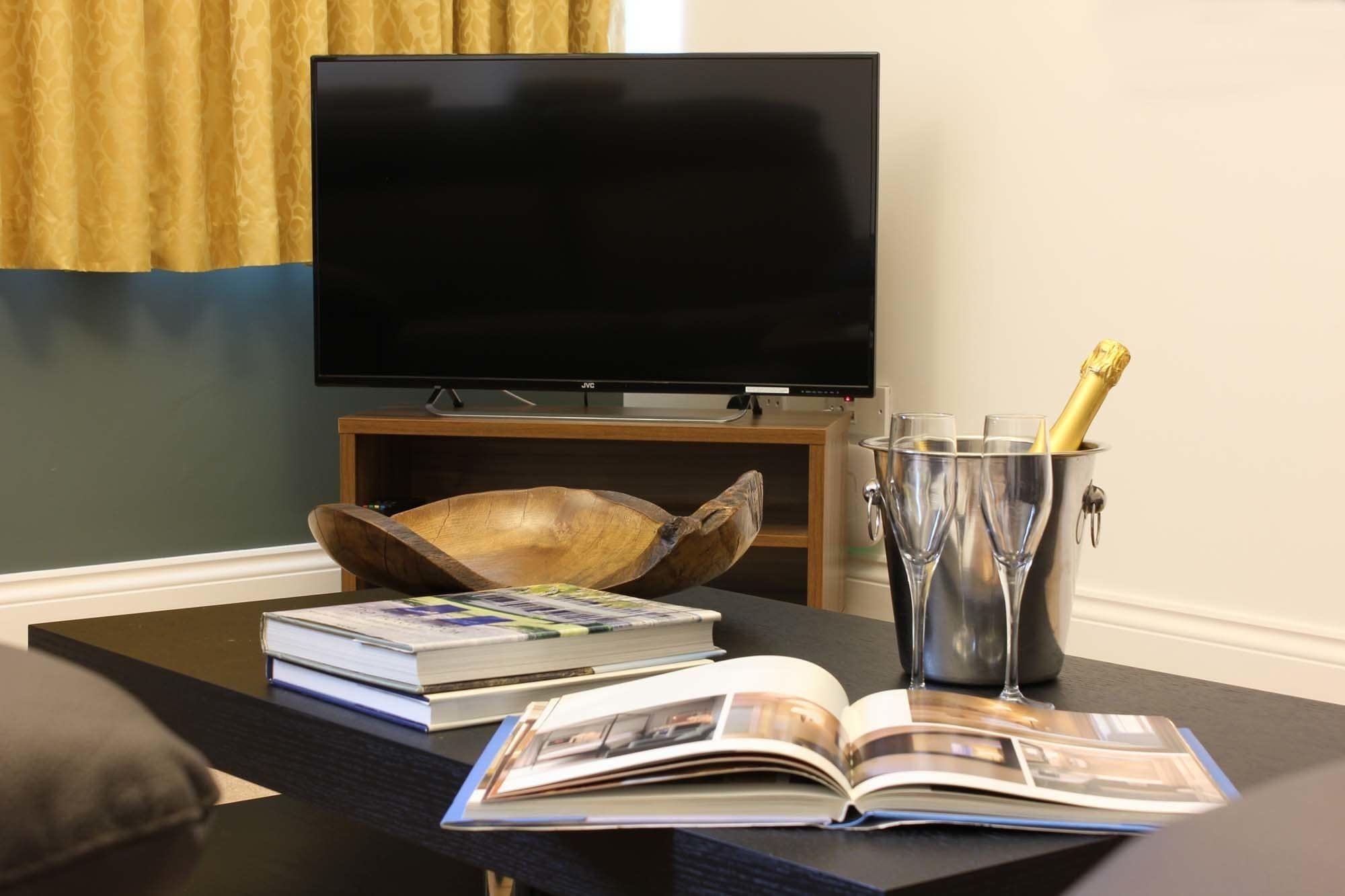 Un salon avec un téléviseur à écran plat, un saladier en bois, un livre, un magazine et une bouteille de champagne dans un seau en métal.