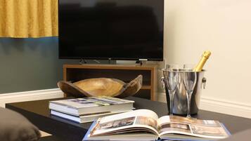 Un salon avec un téléviseur à écran plat, un saladier en bois, un livre, un magazine et une bouteille de champagne dans un seau en métal.
