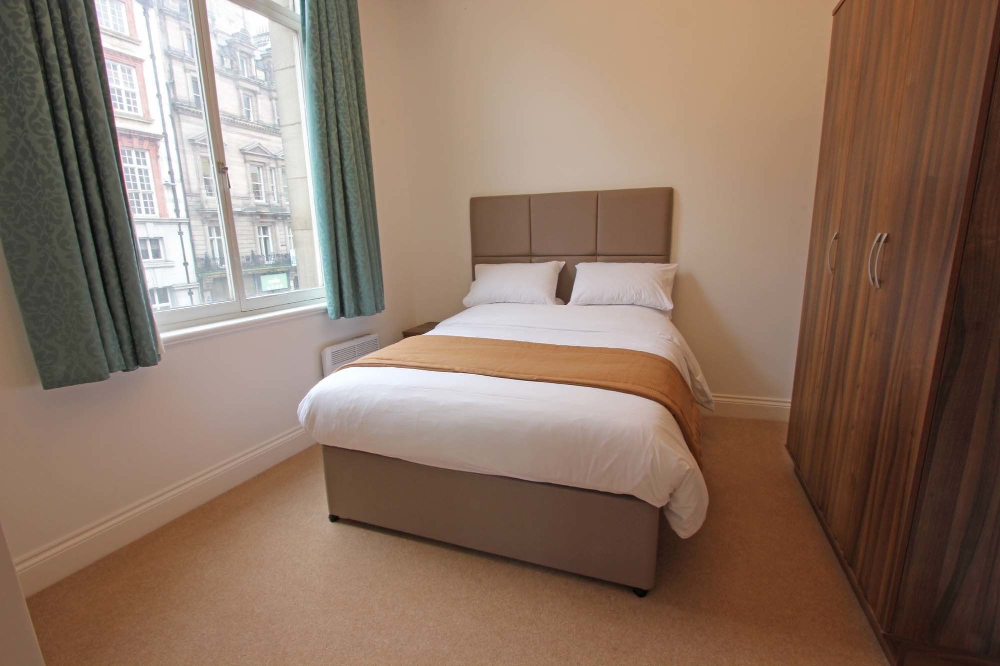 Ein ordentlich eingerichtetes Schlafzimmer mit einem Bett, einem Fenster mit Vorhängen und einem Kleiderschrank.