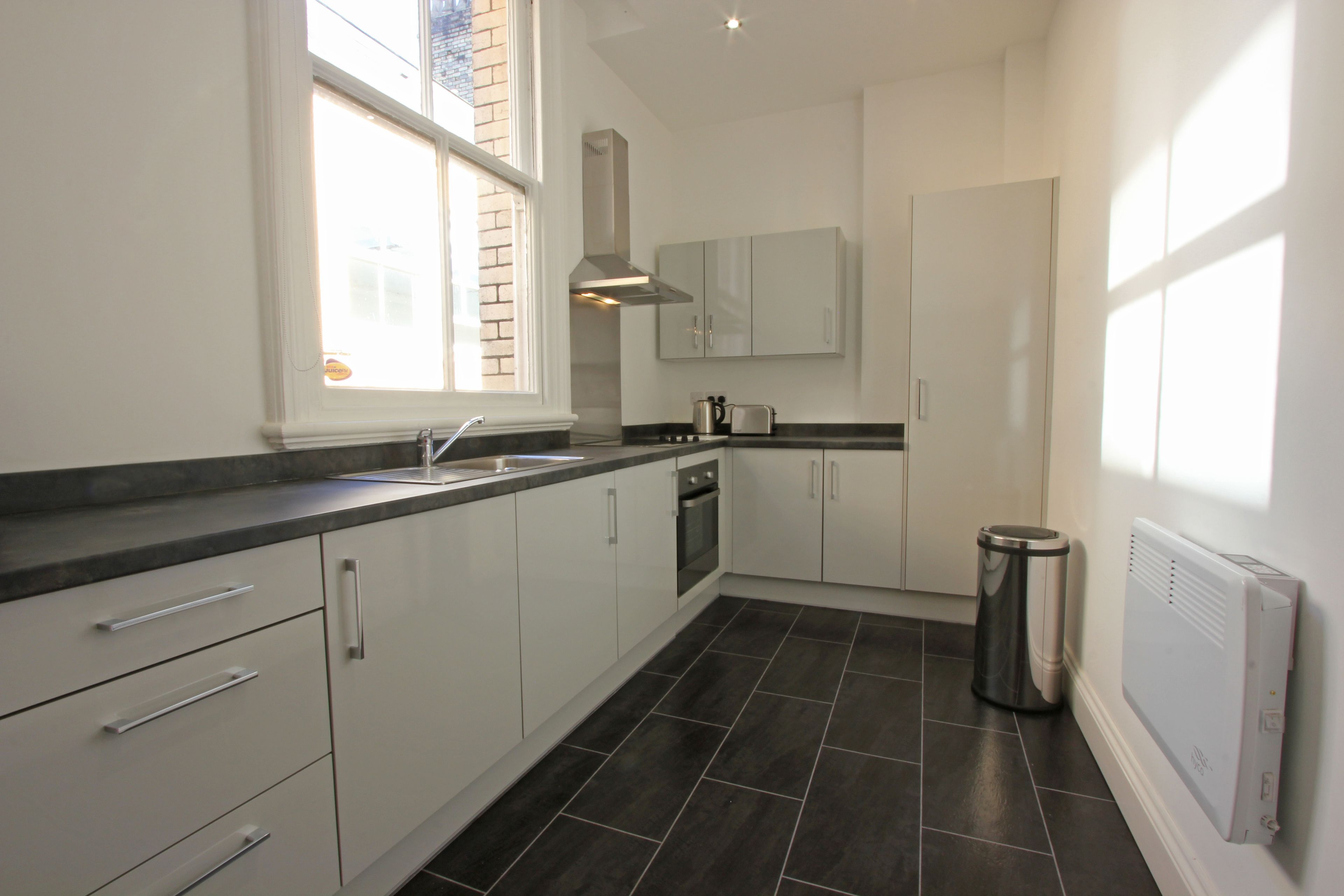 A modern kitchen with white cabinets, a stainless steel range hood, and a black tiled floor.