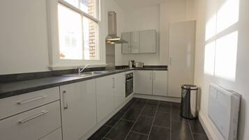 A modern kitchen with white cabinets, a stainless steel range hood, and a black tiled floor.