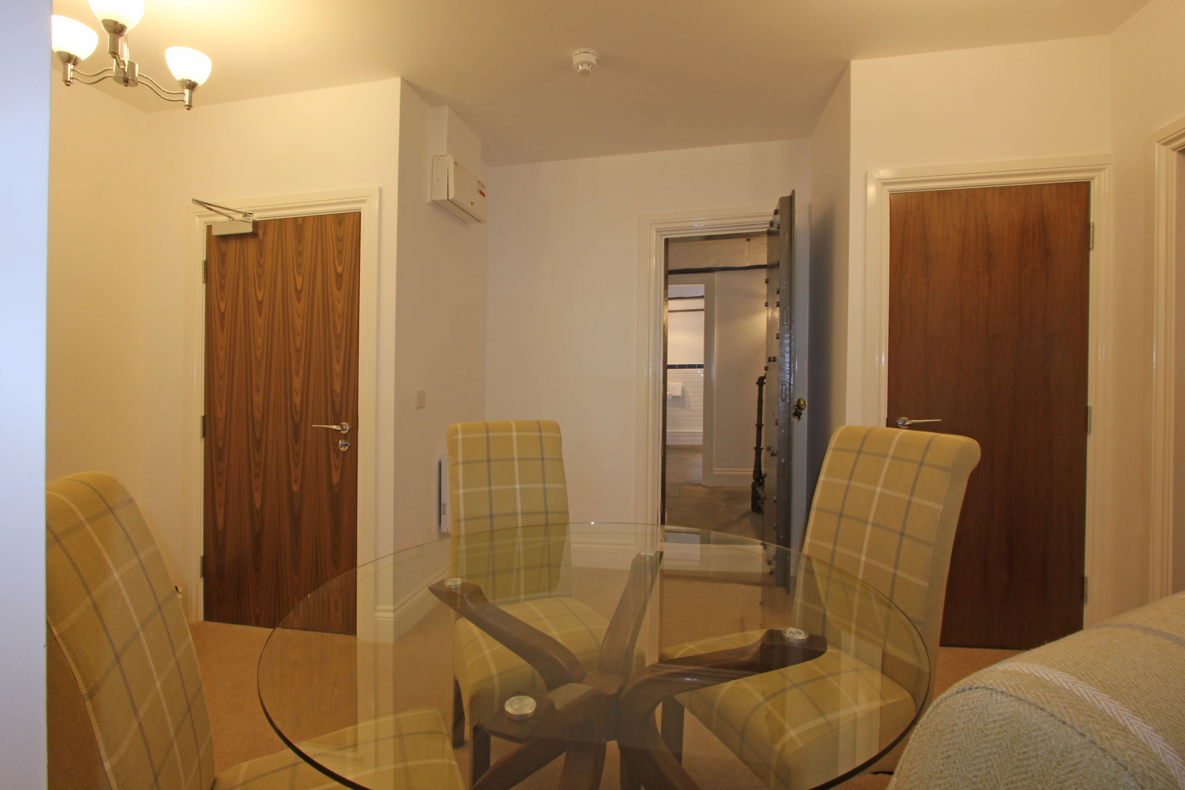 Quarto com mesa de vidro, cadeiras ao redor, portas de madeira e corredor que dá para outro cômodo.