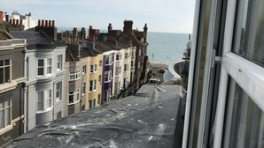 Vista desde una ventana con una hilera de casas coloridas en terraza, y una playa y mar al fondo.