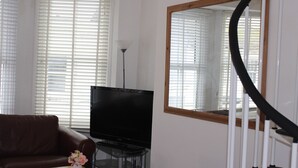 Una sala de estar con un sofá de cuero marrón, una mesa de centro de vidrio, un televisor de pantalla plana y un espejo grande en la pared.