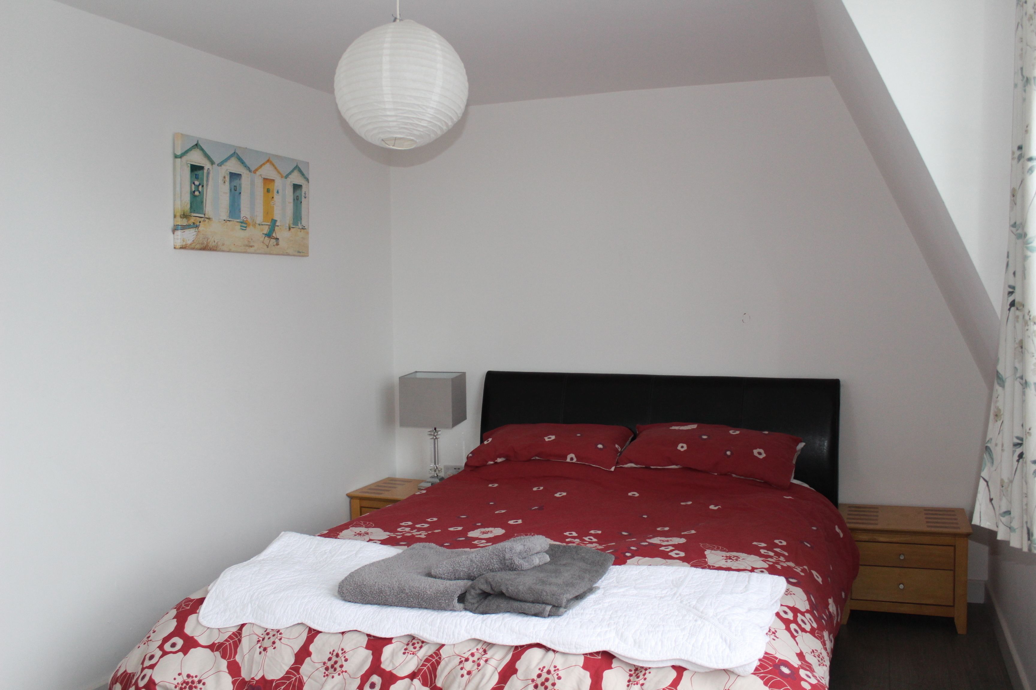 Ein Schlafzimmer mit einem Bett, einem Nachttisch, einer Lampe und einem Bild an der Wand.